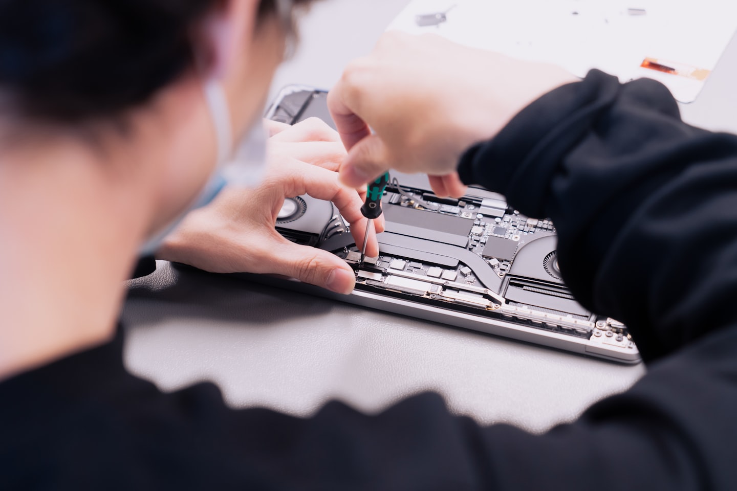 Technician repairing laptop components on a workbench.